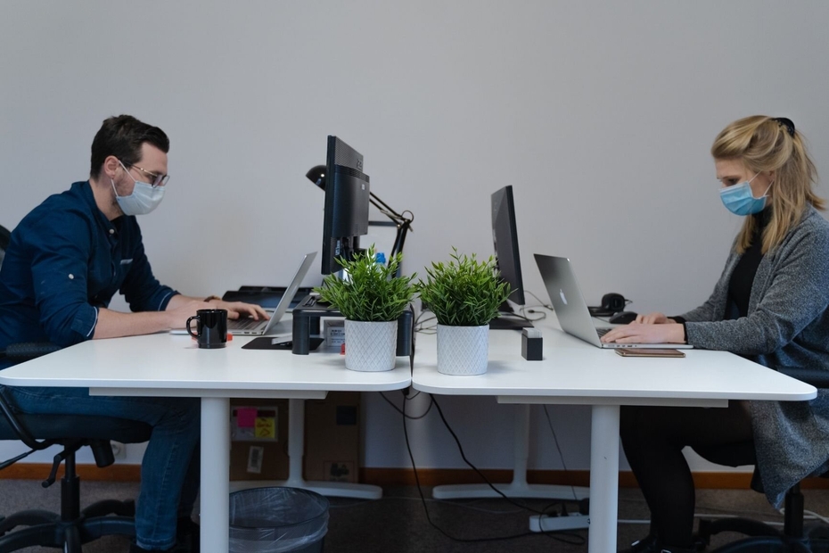 a men and a woman working on computers wearing masks